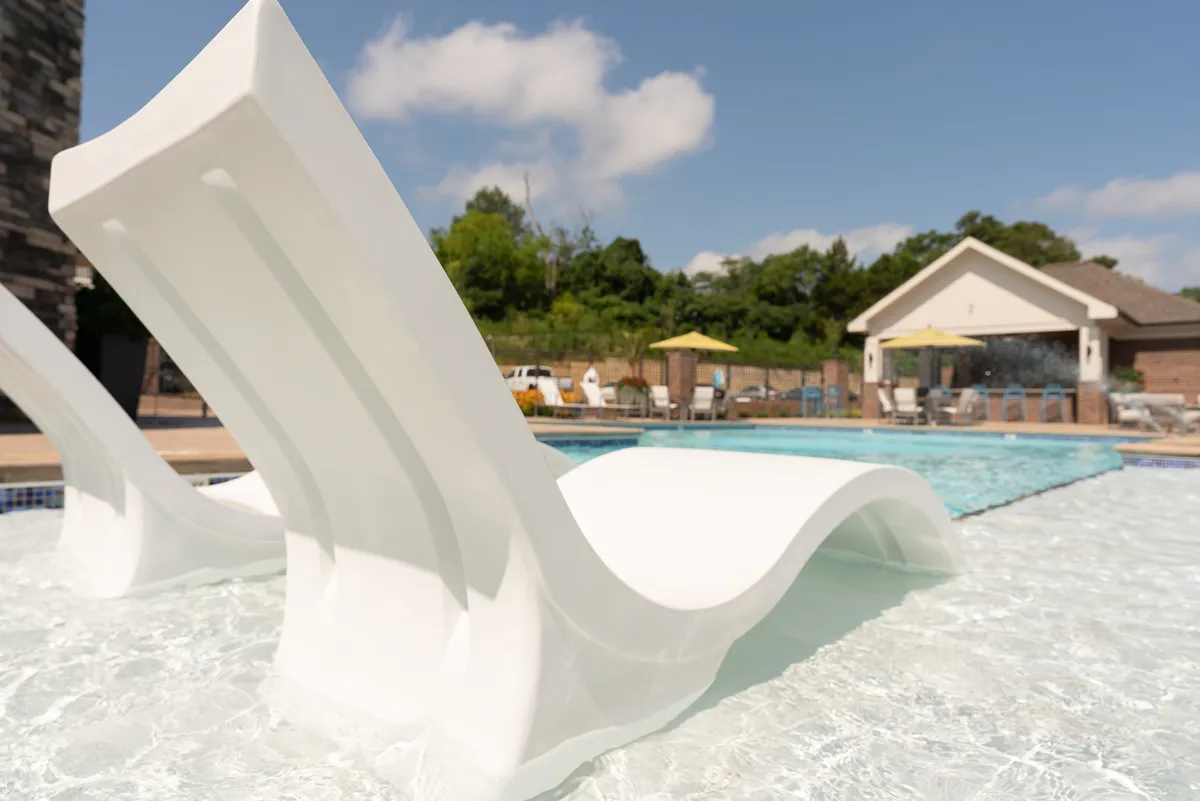 A tranquil exterior scene featuring a sparkling swimming pool surrounded by lush greenery, poolside lounge chairs, and a shaded cabana. The setting invites guests to relax, socialize, or enjoy a sun-filled afternoon just steps from home.