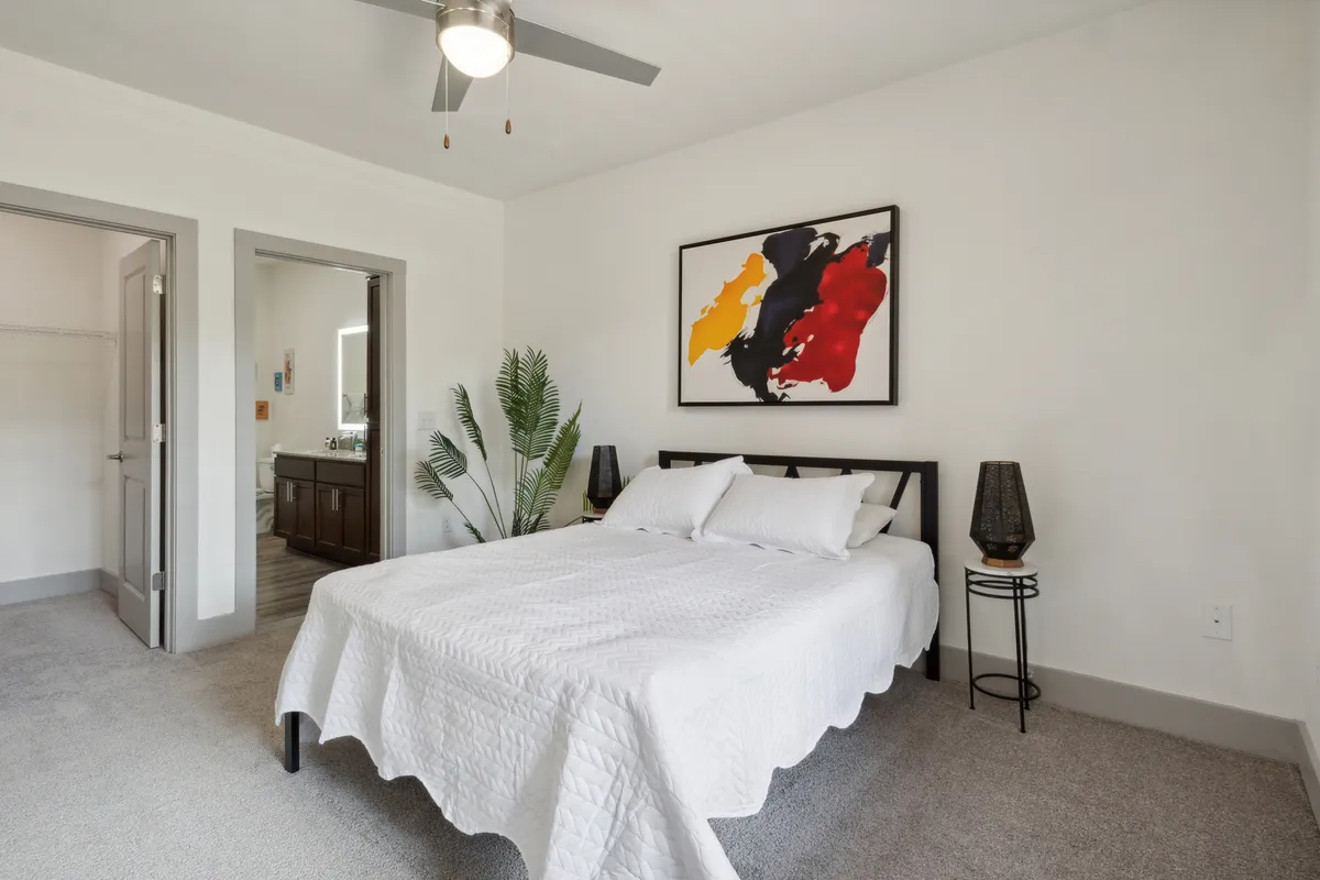 A contemporary bedroom featuring a stylish bed with crisp linens, abstract artwork above the headboard, a potted plant for a touch of greenery, and a nightstand. Soft natural light filters through the window, creating a calm and inviting atmosphere ideal for unwinding after a day of exploring Knoxville.