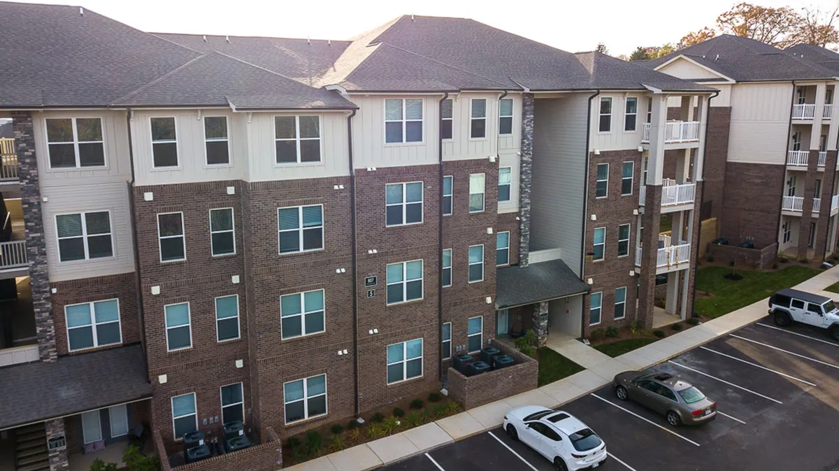 A welcoming brick facade with large windows and an entrance awning, complemented by a clearly visible parking area. The scene exudes a sense of accessibility and warmth, suggesting a vibrant, well-located residential community.