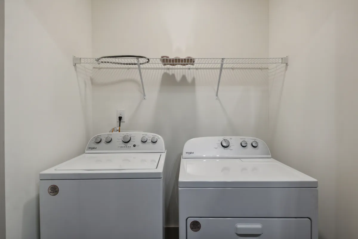 A dedicated laundry area with a washing machine, dryer, and a practical shelf for organization. The space is tidy and functional, reinforcing the convenience of in-unit amenities.