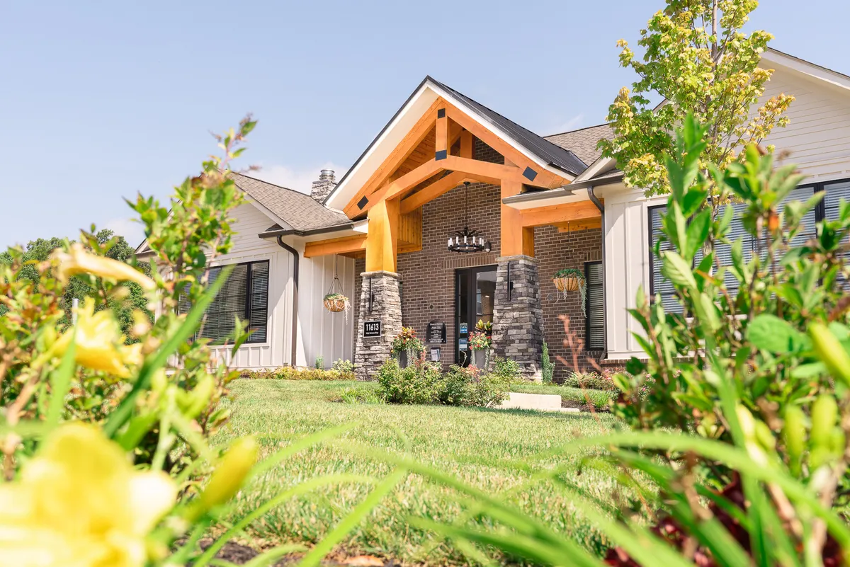 A wooden entryway with sturdy stone pillars and a beautifully landscaped garden, inviting residents to gather, relax, or enjoy the outdoors. The area is set up for both peaceful solitude and social gatherings.