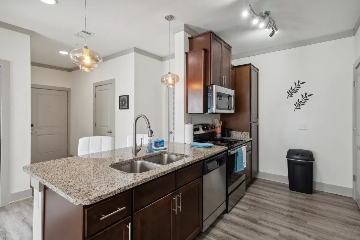 This image captures a modern kitchen with a granite countertop, stainless steel appliances, a central kitchen island, and stylish pendant lighting. Decorative wall elements add a touch of personality, while the space is open and inviting, ideal for both cooking and socializing.