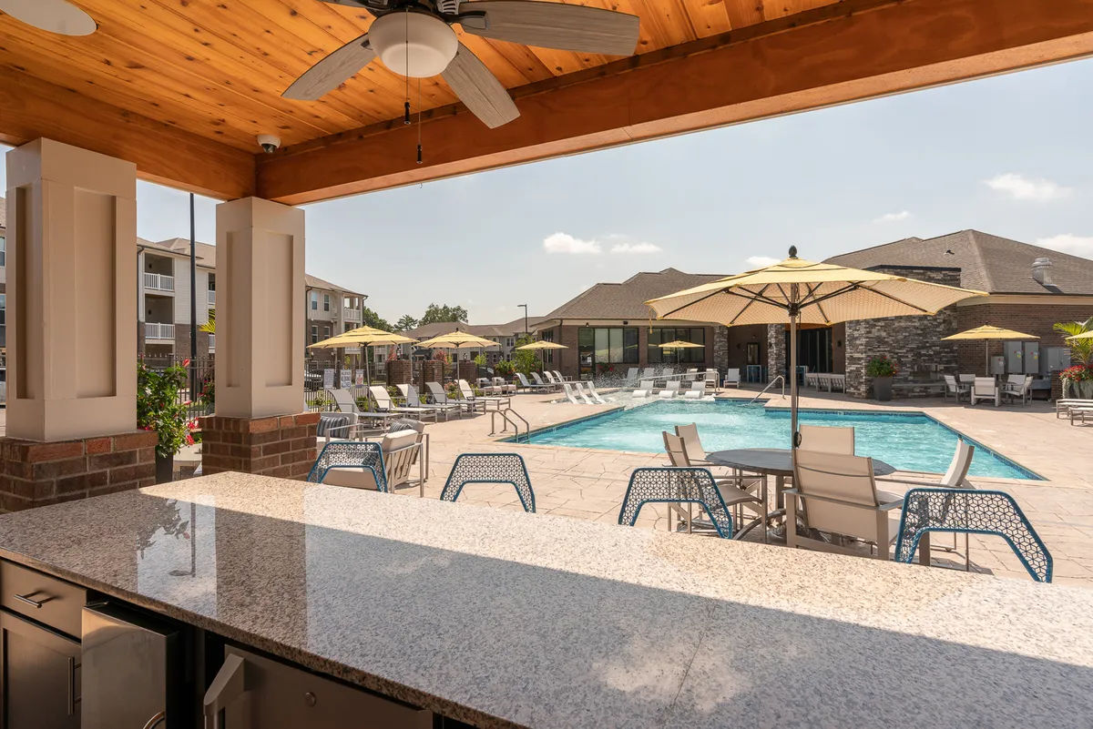 An energetic exterior view of the pool with vibrant umbrellas, an outdoor seating area, and a stylish bar counter. The space is designed for both active days in the sun and memorable gatherings with friends and family.