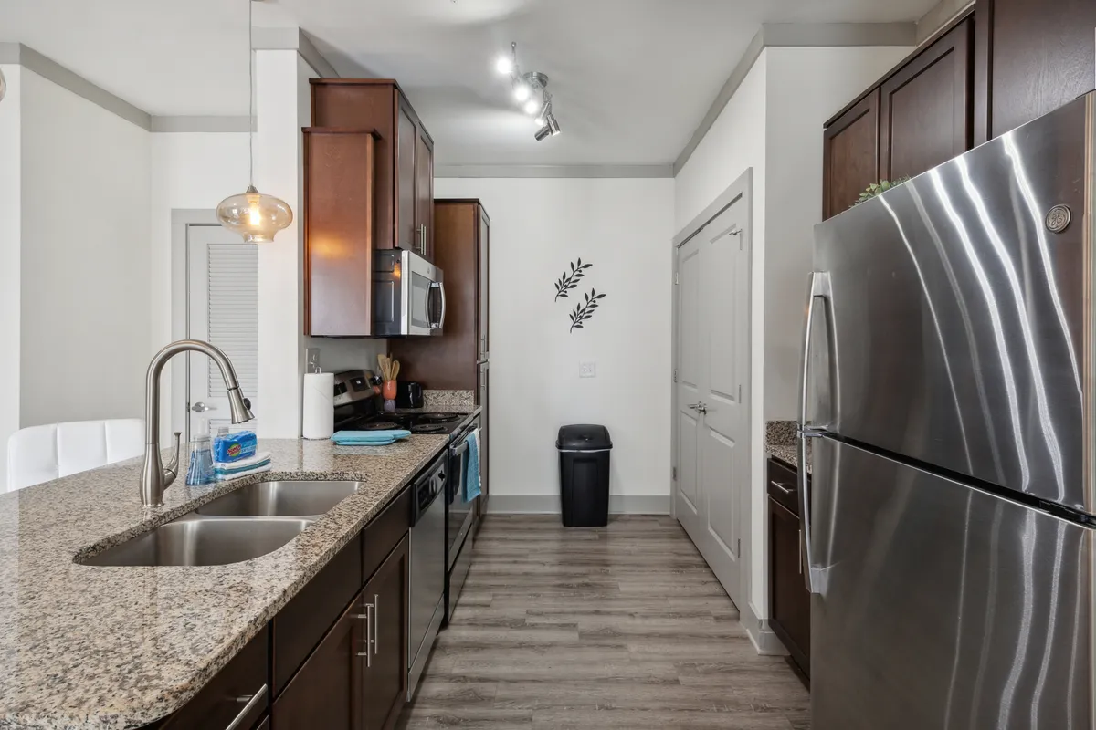 A bright, inviting kitchen scene featuring a granite countertop, stainless steel appliances, and decorative wall foliage. The layout encourages both cooking and hosting, signaling the space's flexibility for family meals or dinner parties.