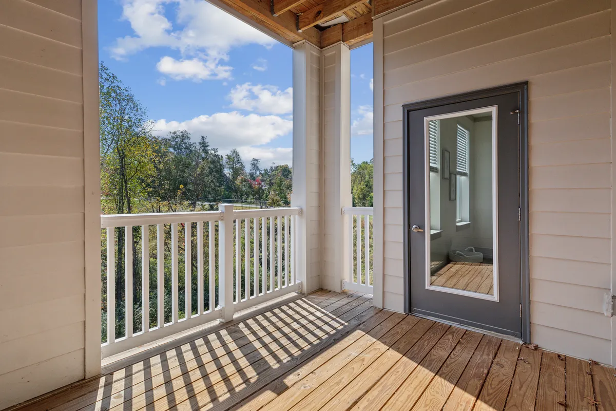 A serene wooden deck framed by a white railing and a door with a mirror, ideal for relaxing with morning coffee, enjoying fresh air, or unwinding after work. The natural surroundings and tranquil atmosphere are evident.