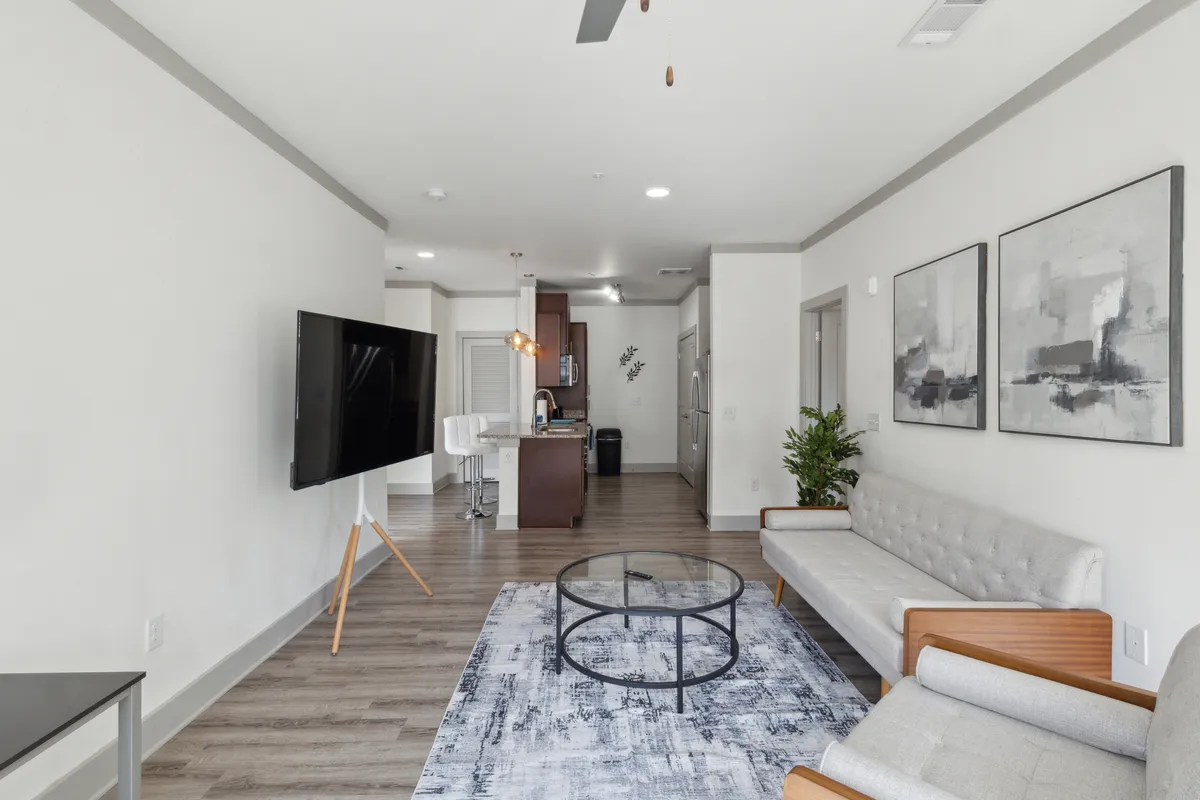 A contemporary living area showcasing a cozy sofa, coffee table, wall-mounted television, and eye-catching artwork. The room exudes a comfortable vibe, with modern decor and ample lighting making it perfect for relaxation and socializing.