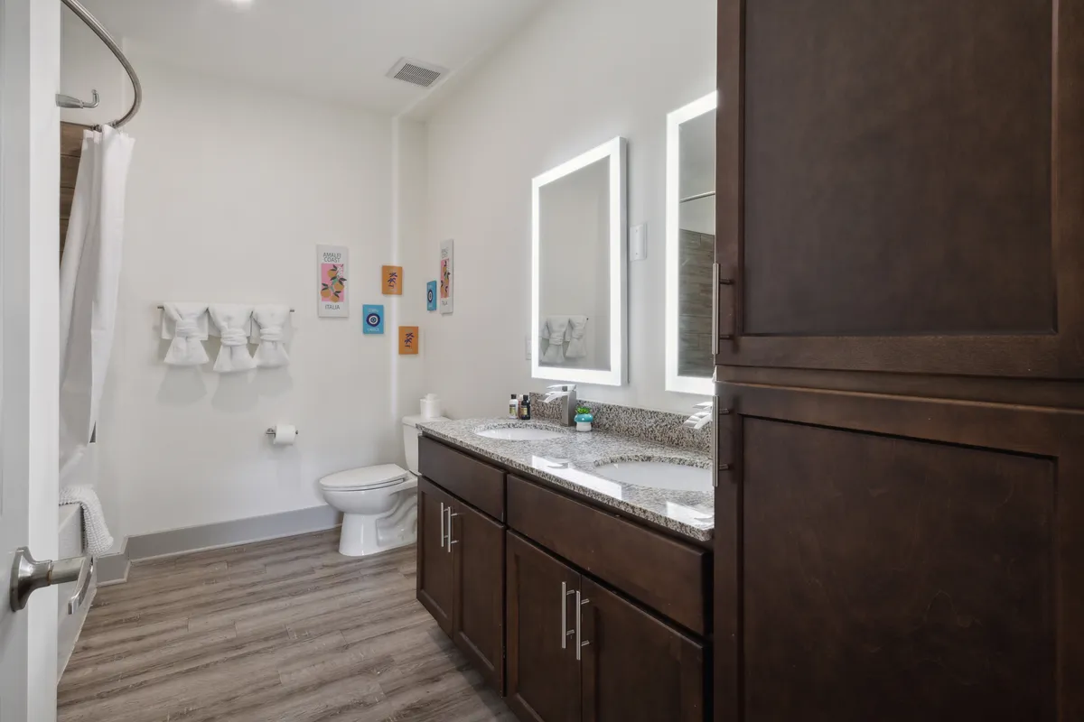 A modern bathroom with a double sink vanity, illuminated mirrors with backlighting, granite countertops, and a neatly arranged towel rack. The space is bright, fresh, and thoughtfully designed for relaxing morning or evening routines.